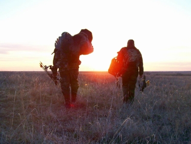 Two hunters cross a prairie at sunrise