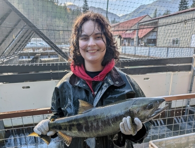 WaterCorps Service Member holding an adult chum salmon. Fish hatchery and skyline in the background.