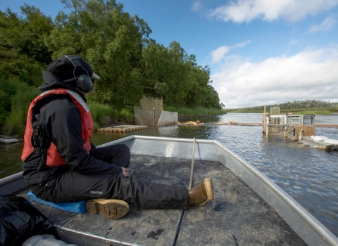 person in PFD on a boat approaching a weir structure across a river