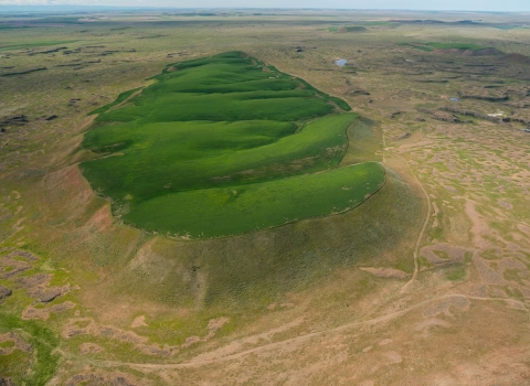 Crops of wheat growing on the top of a flood-carved mesa are a green contrast to the surrounding drier landscape.