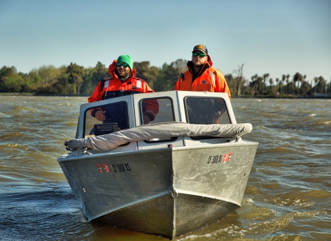Two men pilot a motored boat on a river