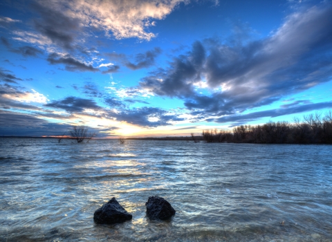 Sun just below horizon over lake with dramatic clouds above.