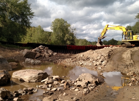 muddy, rocky riverbed with excavator on hill on right