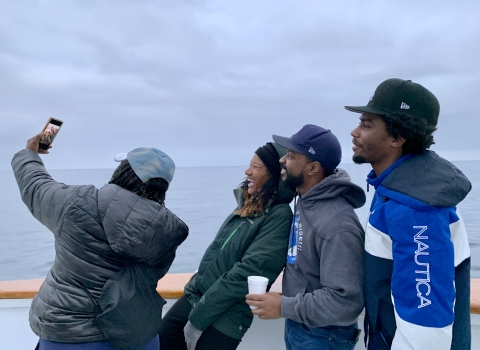 Four members of the organization stand next to each other and take a selfie. The ocean view is in the background. 