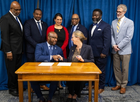 6 dressed up people behind 2 at table shaking hands