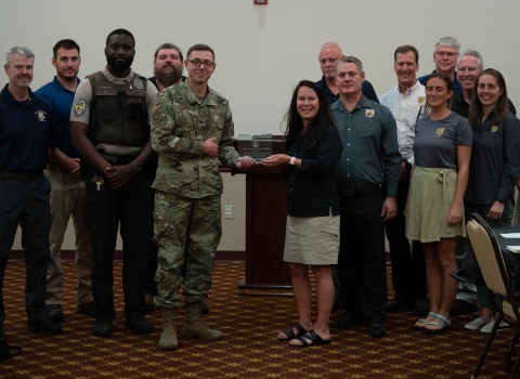 A man in fatigues accepts an award from a woman in a U.S. Fish and Wildlife Service shirt with a group of other people standing around them