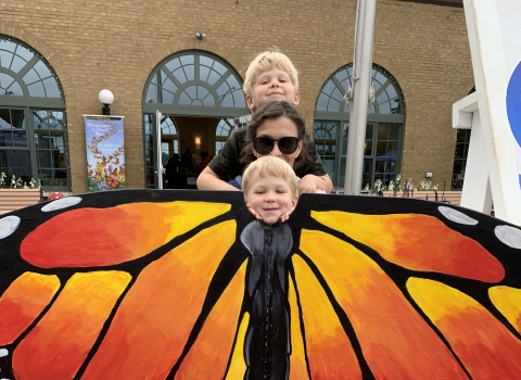 2 small children pose and adult behind a monarch butterfly cutout