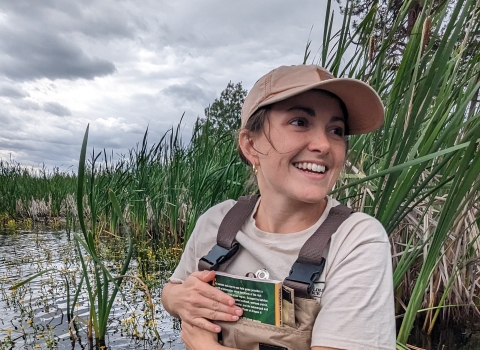 A biologist holds field guides close while wading into a wetland.
