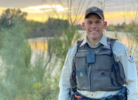 a uniformed officer poses for a picture at the edge of a Southern Texas landscape 