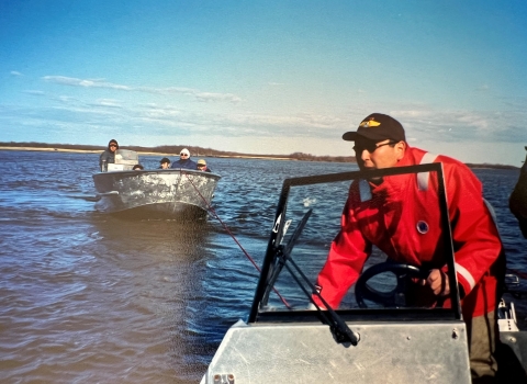 a federal officer at the helm of a river boat drives as his boat is tied to another boat with a family of five people