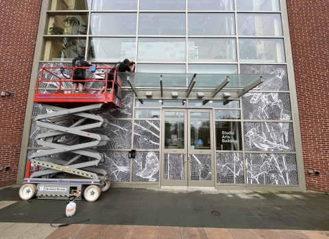 Two people on a construction lift apply decals to the front of a building