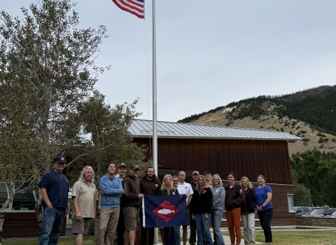 2 UHS flags fly and at base of flagpole, people pose with fish flag