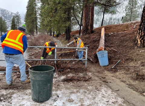 three people in safety vests move small woody debris into into large trash cans at the LNFH ADA fishing platfoorm