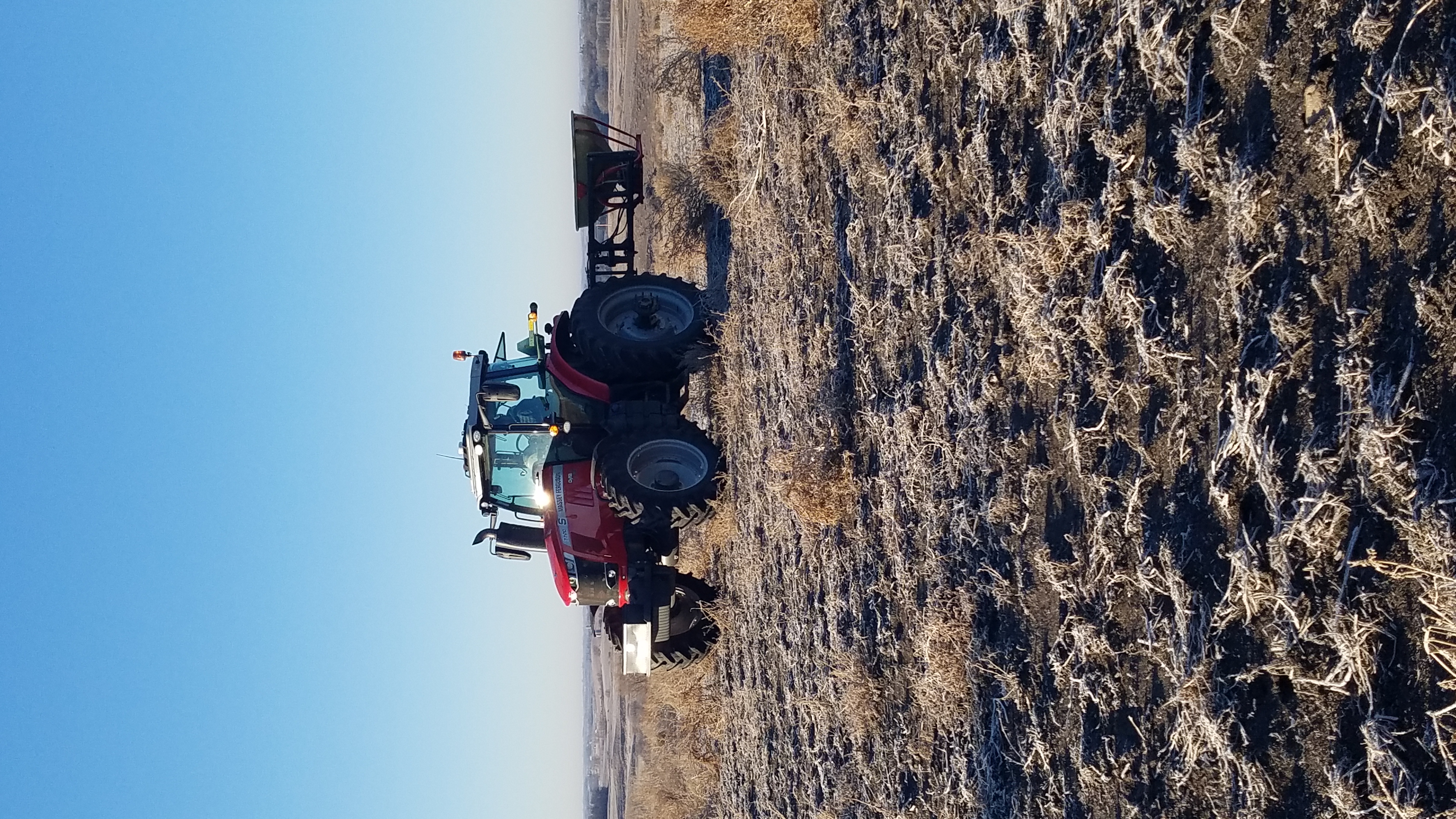 A small tractor pulls a seed spreader across a prairie restoration site