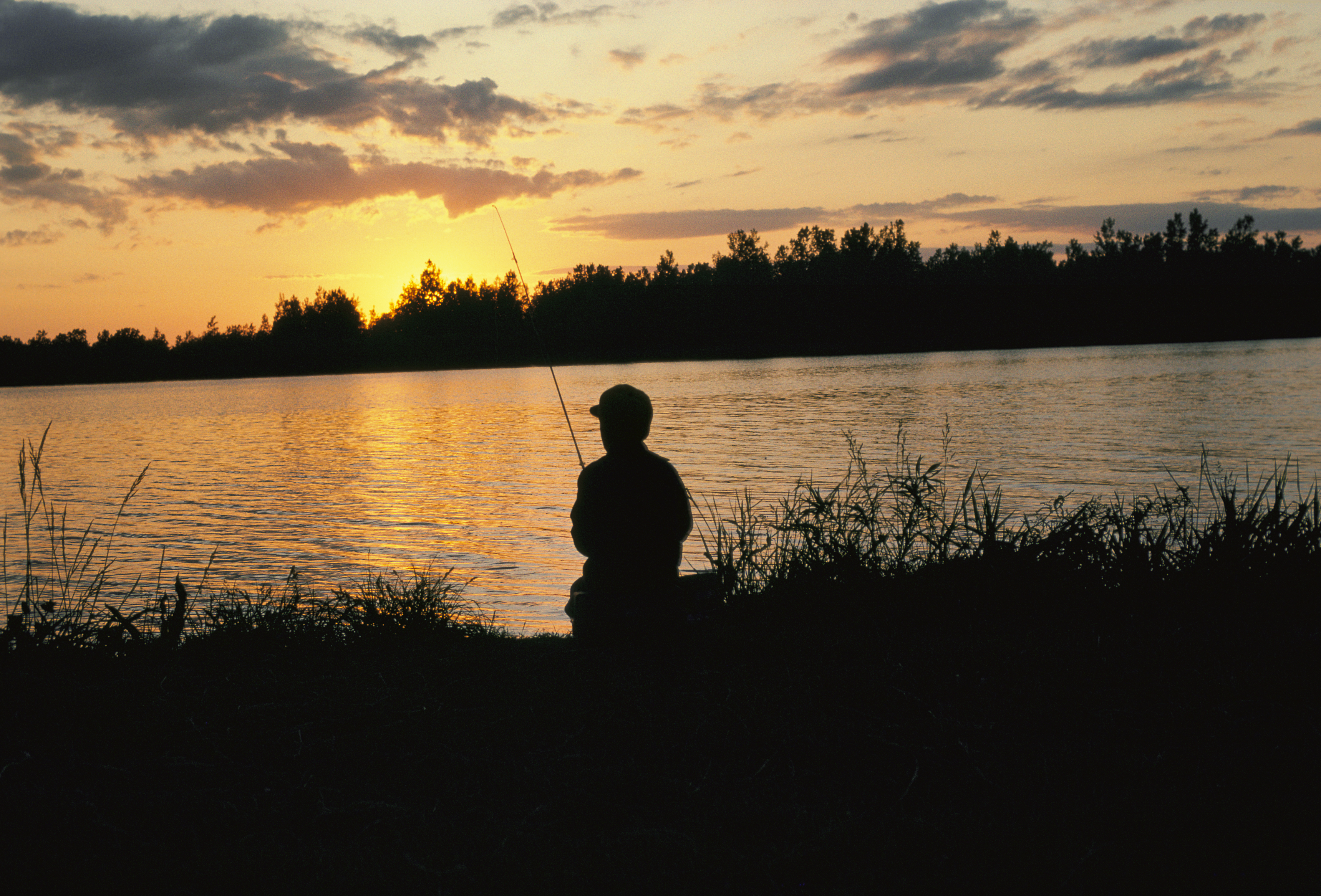 A fishing child's silhouette in front of DeSoto lake at sunset.