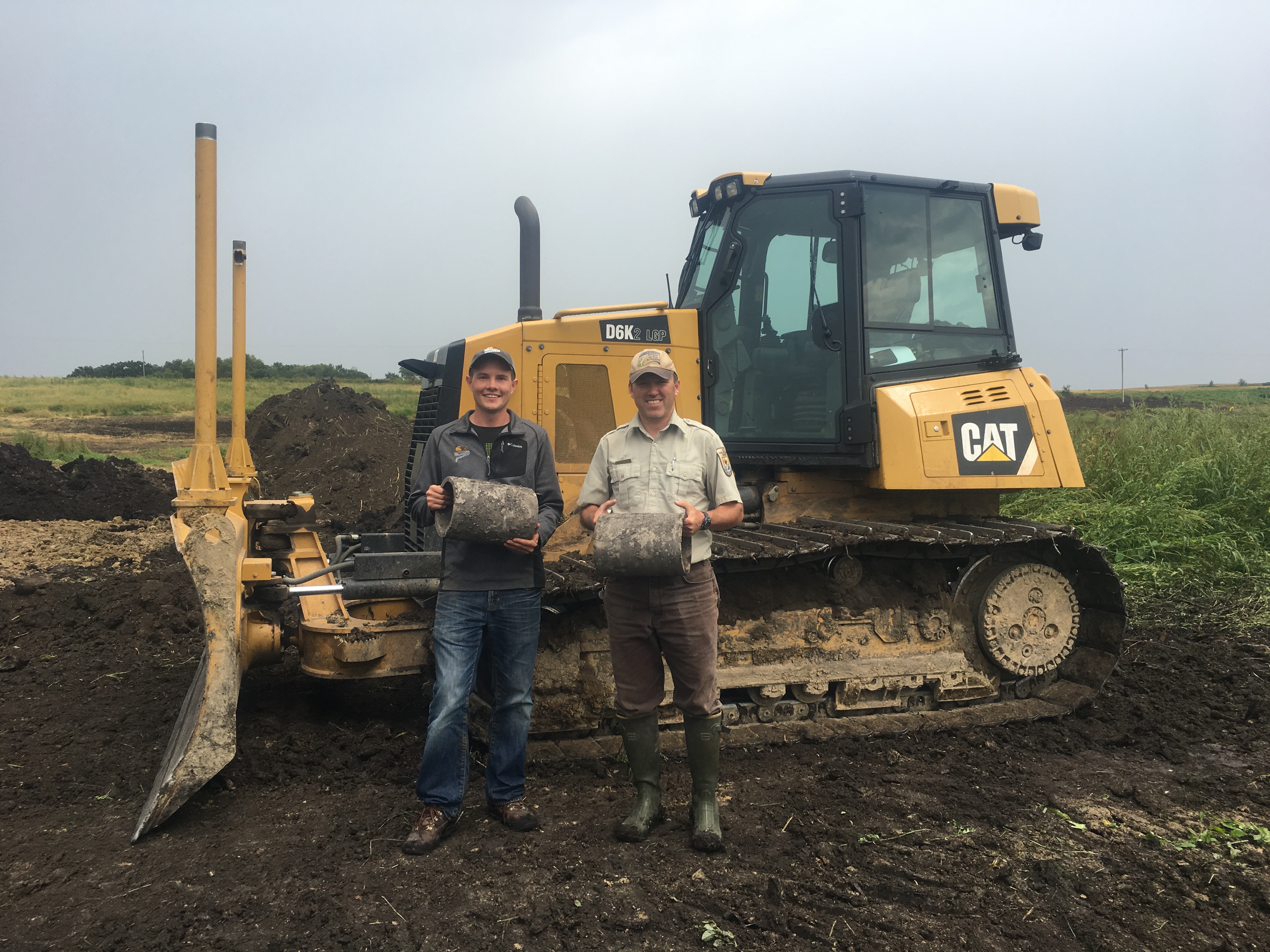 Two staff standing in front of an D6 bulldozer hold concrete tile broken and removed from a drained wetland Nicholson Waterfowl Production Area.