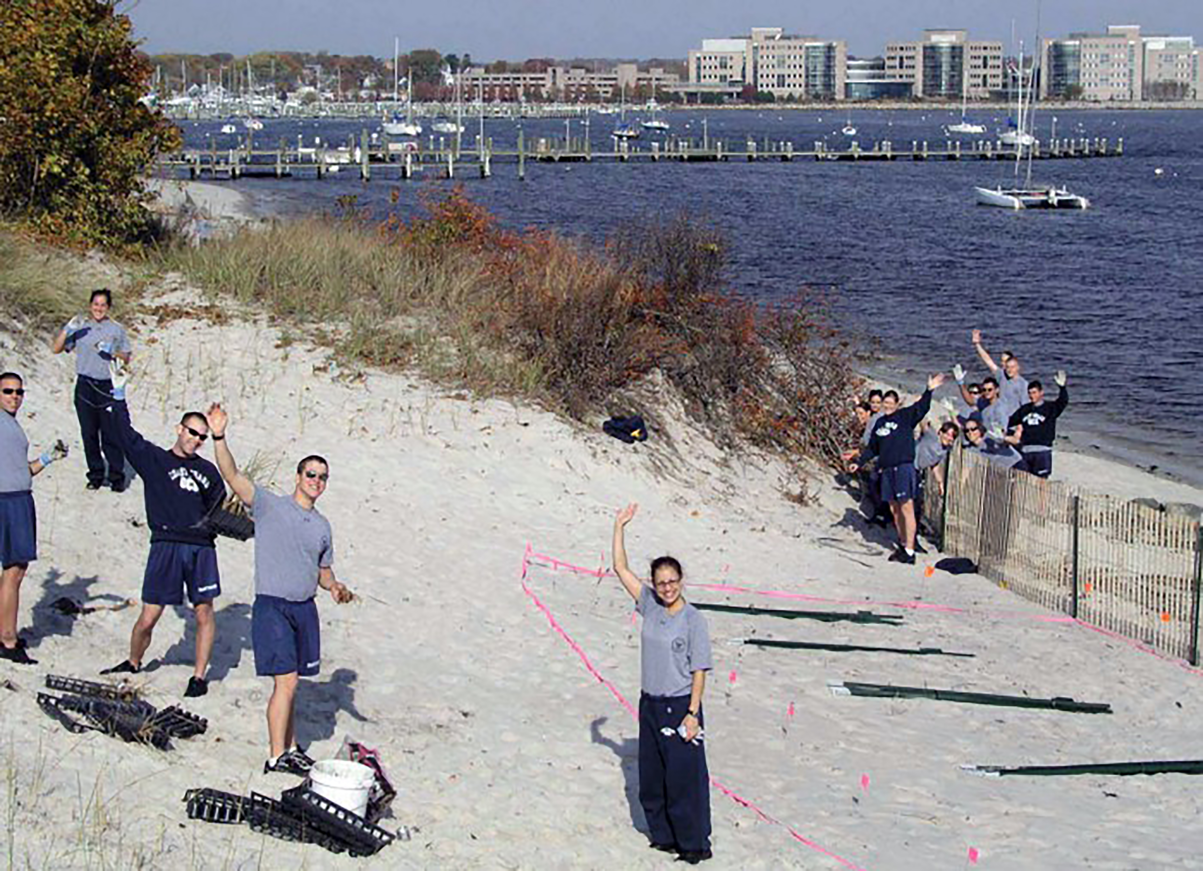 U.S. Coast Guard Academy volunteers standing and waving on sand dunes in New London, CT