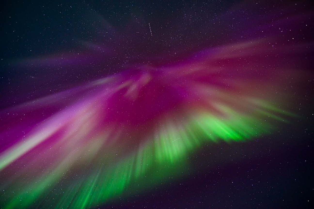 Purples and greens of the Aurora Borealis shine in the black Arctic night sky.