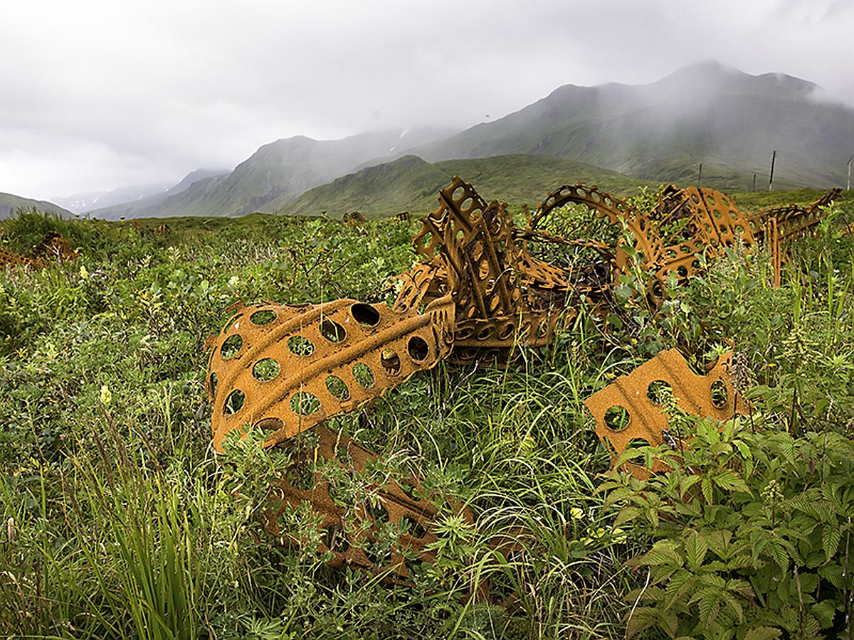 Rusted, perforated sheet metal lying in a field of green vegetation with mountains and fog in the background