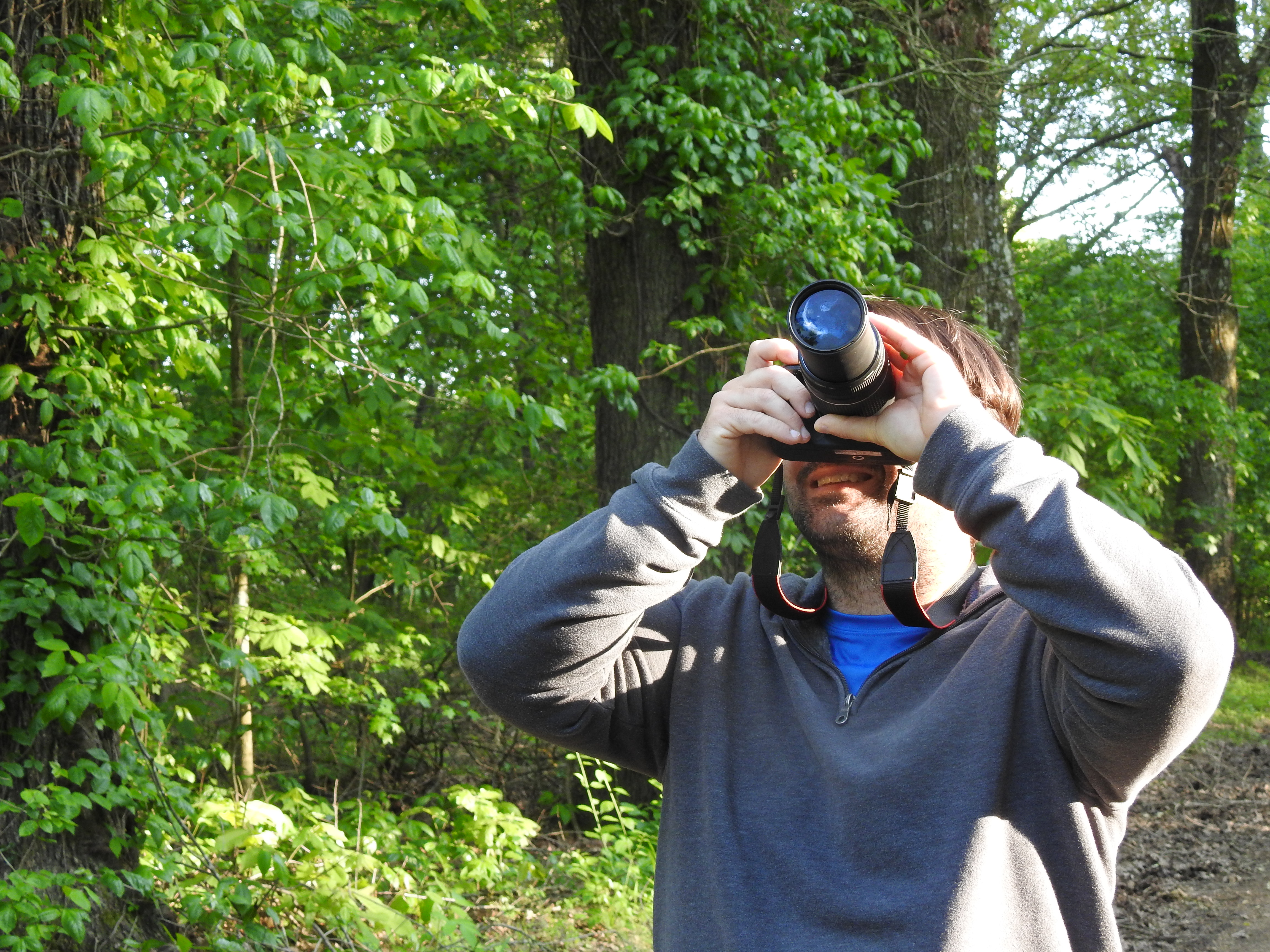 An adult taking a picture in the woods.