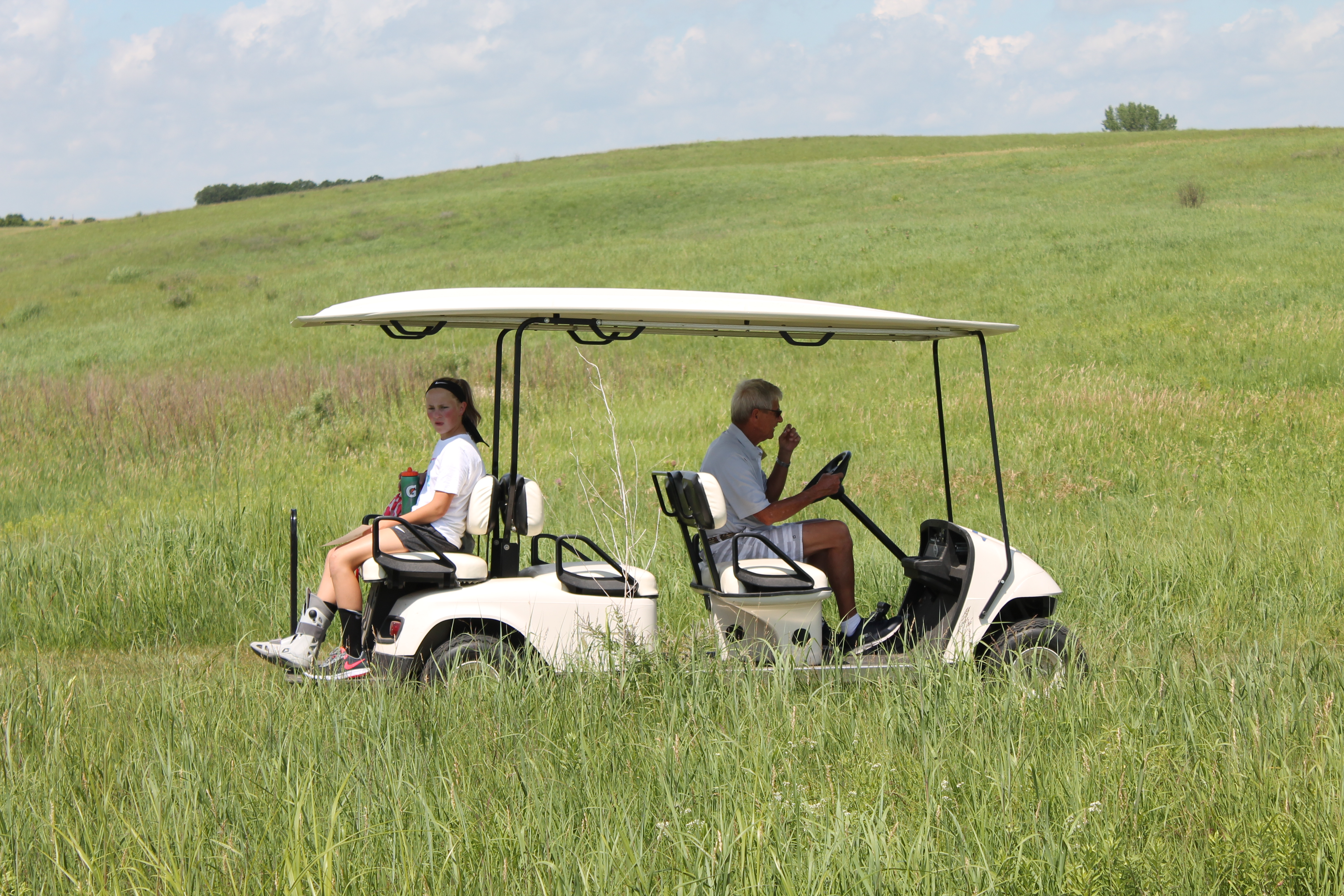 A camper with a cast rides the golf cart on the trails through the summer prairie.