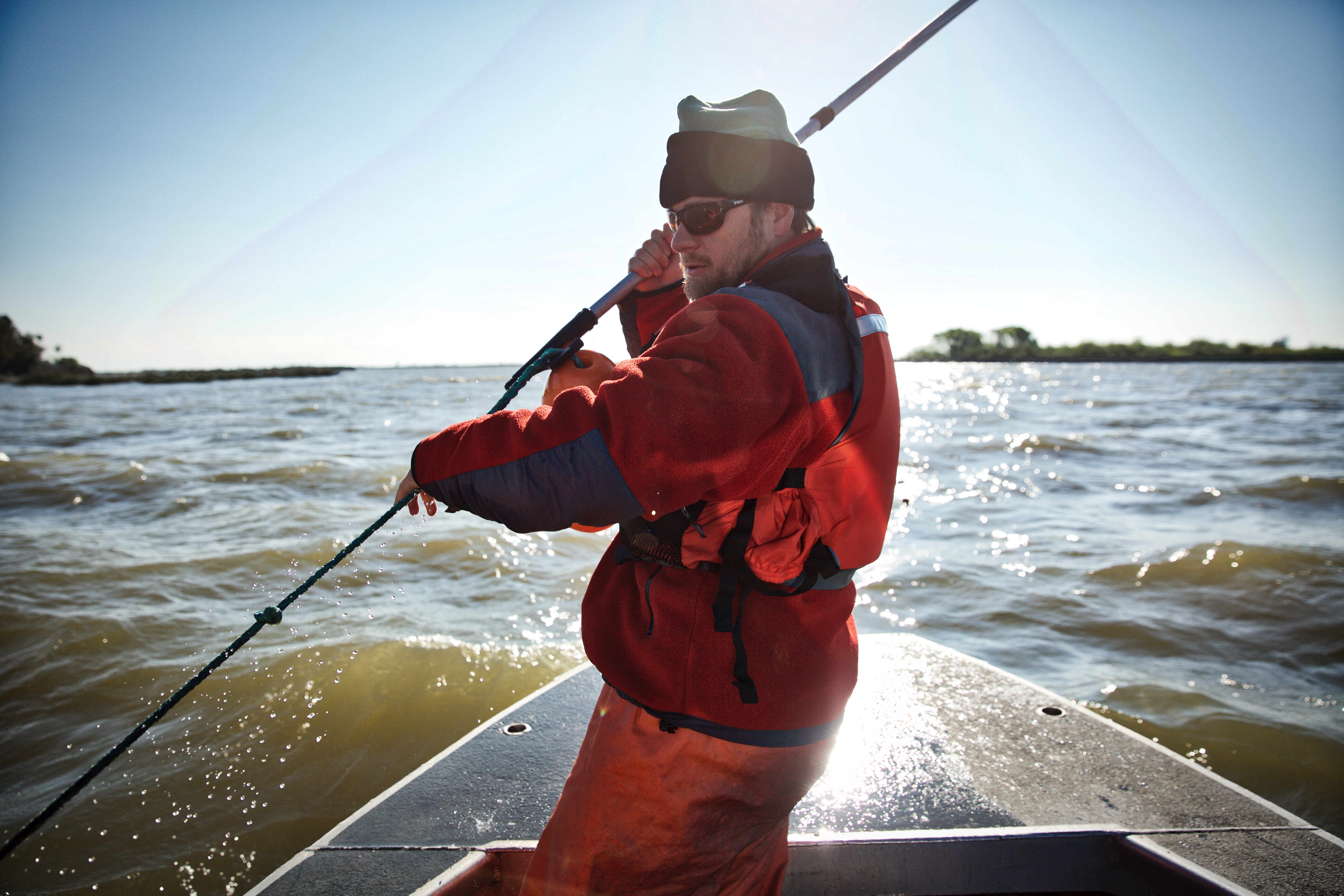 A man on a boat uses a pole to pull in the line of a trawl net