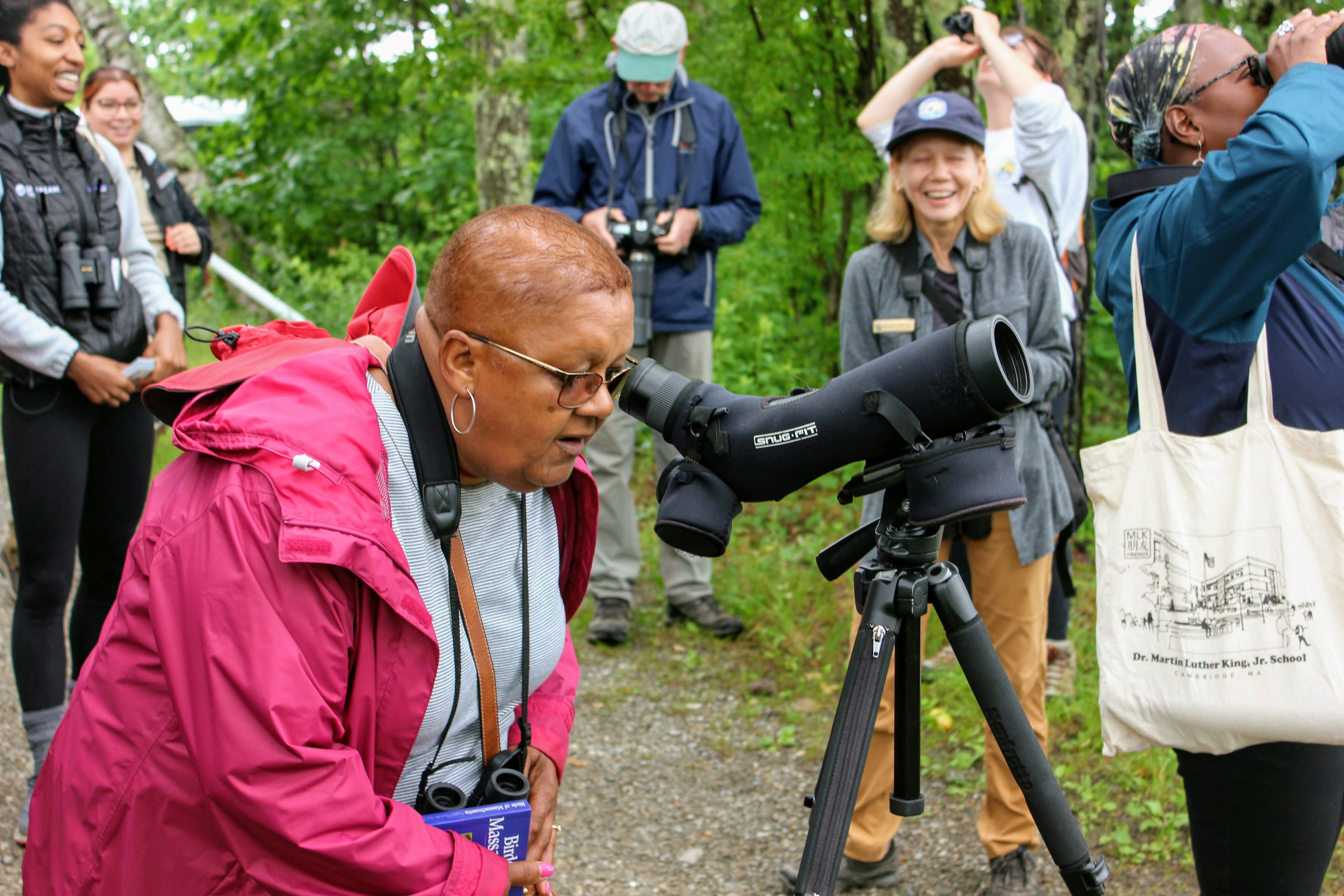 A group of birders, focused on one member looking through a scope