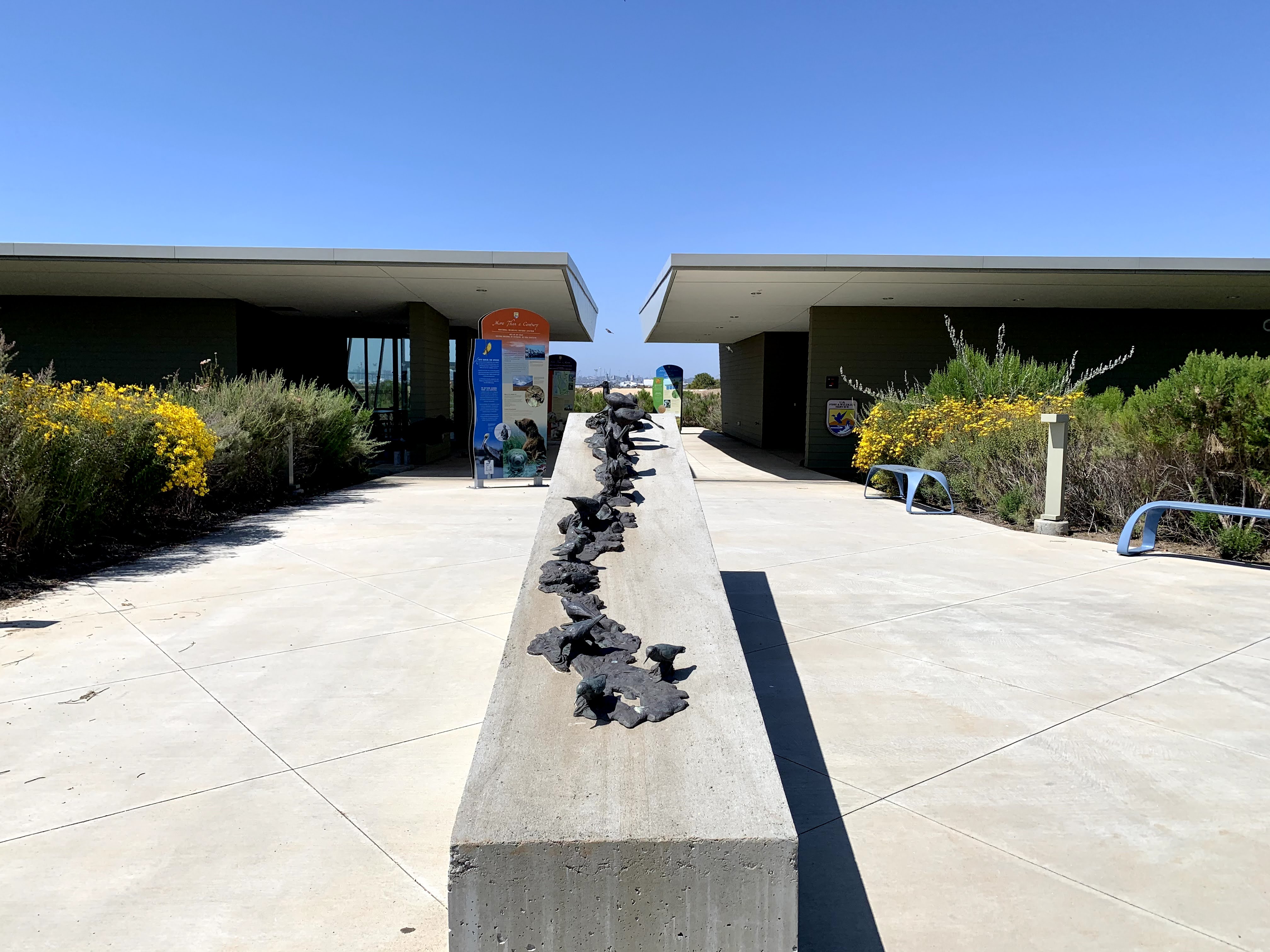 Two buildings with breezeway in between. A block with metal birds is in front of the buildings. 