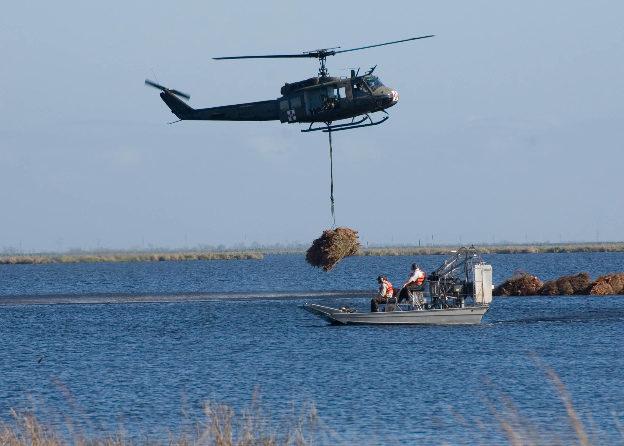 Helicopter drops bundle of trees into open water as an airboat stands by to help