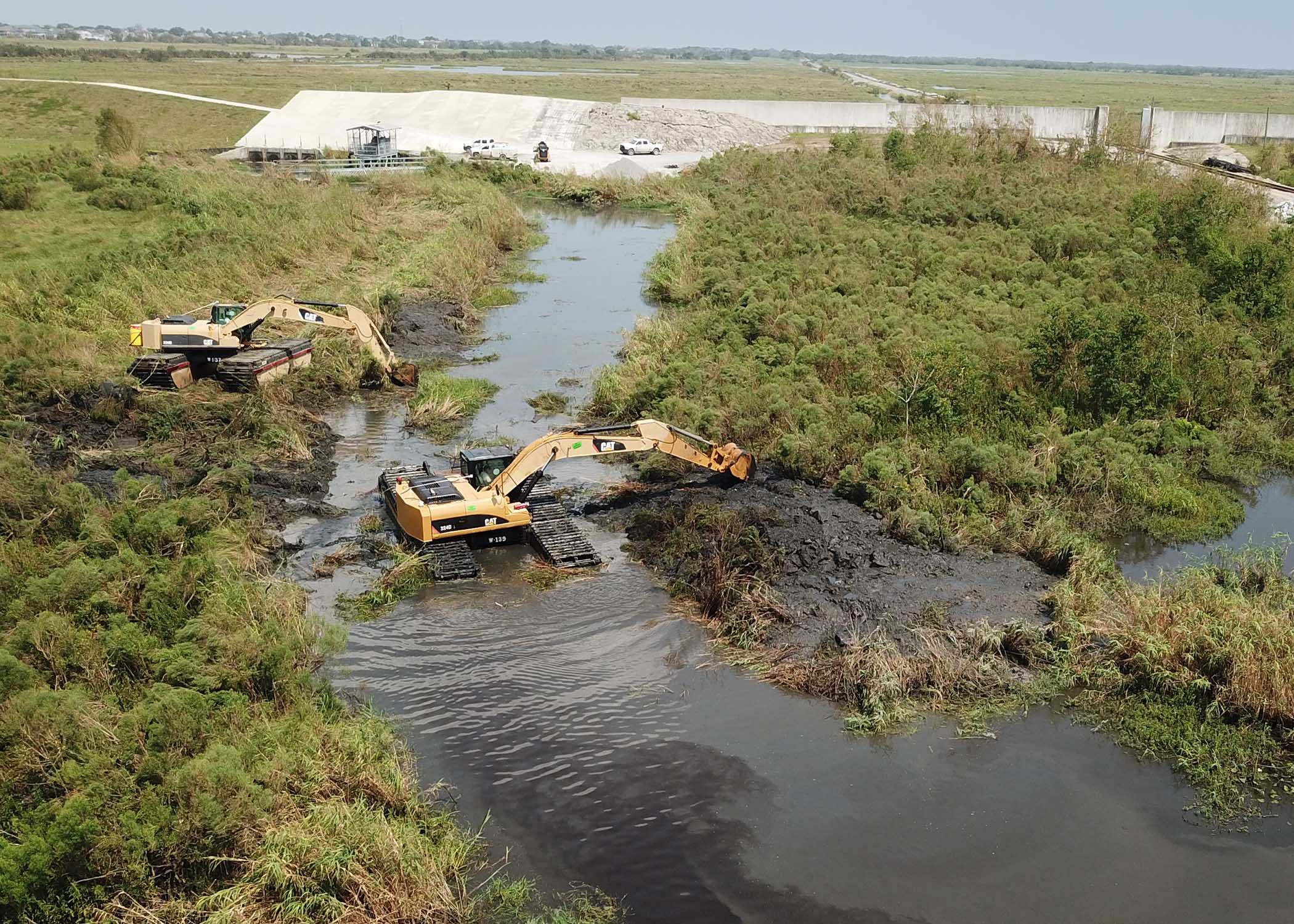 Dredges maintaining water control channel near hurricane protection levee.