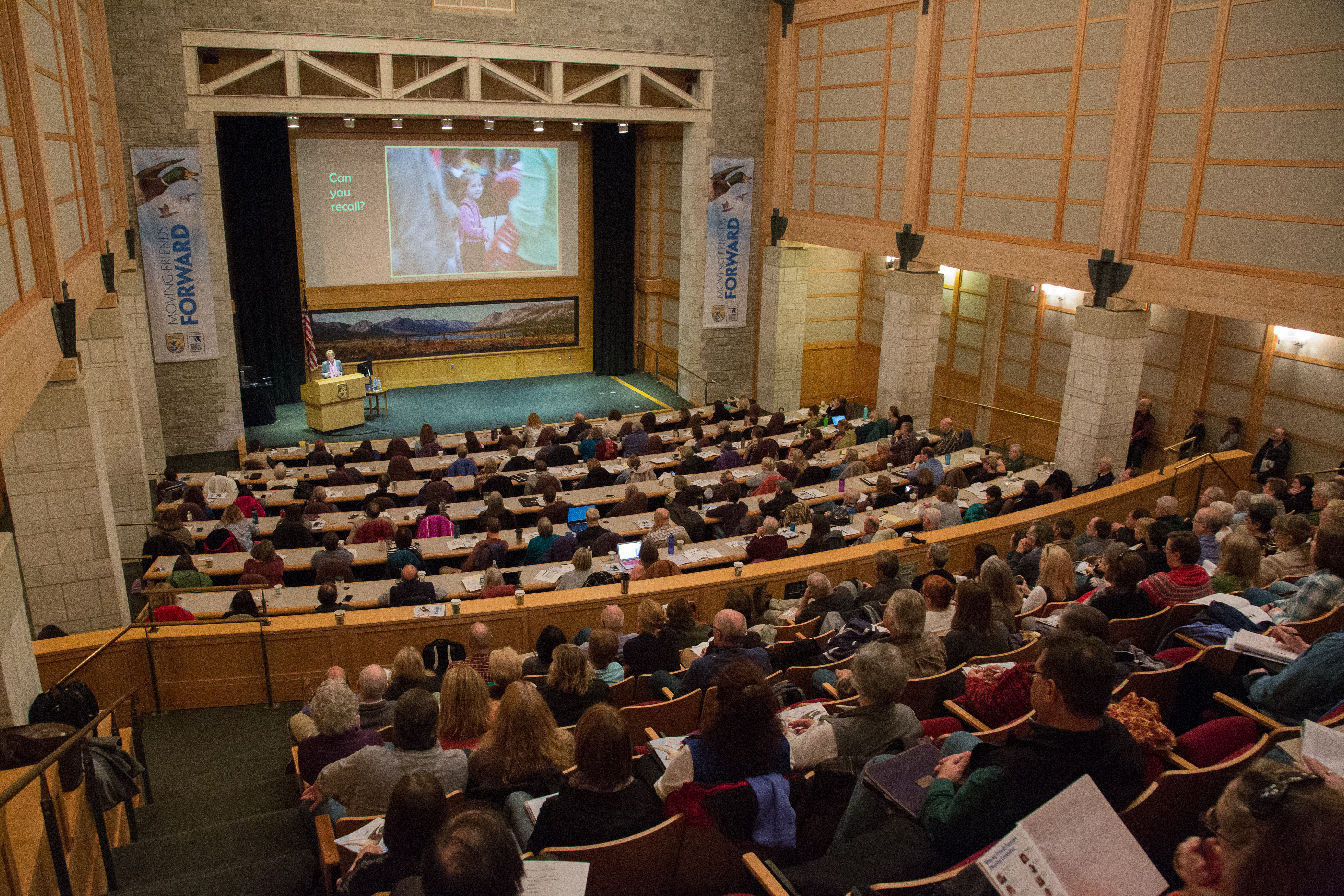 auditorium filled with people viewing presentation on large projection screen