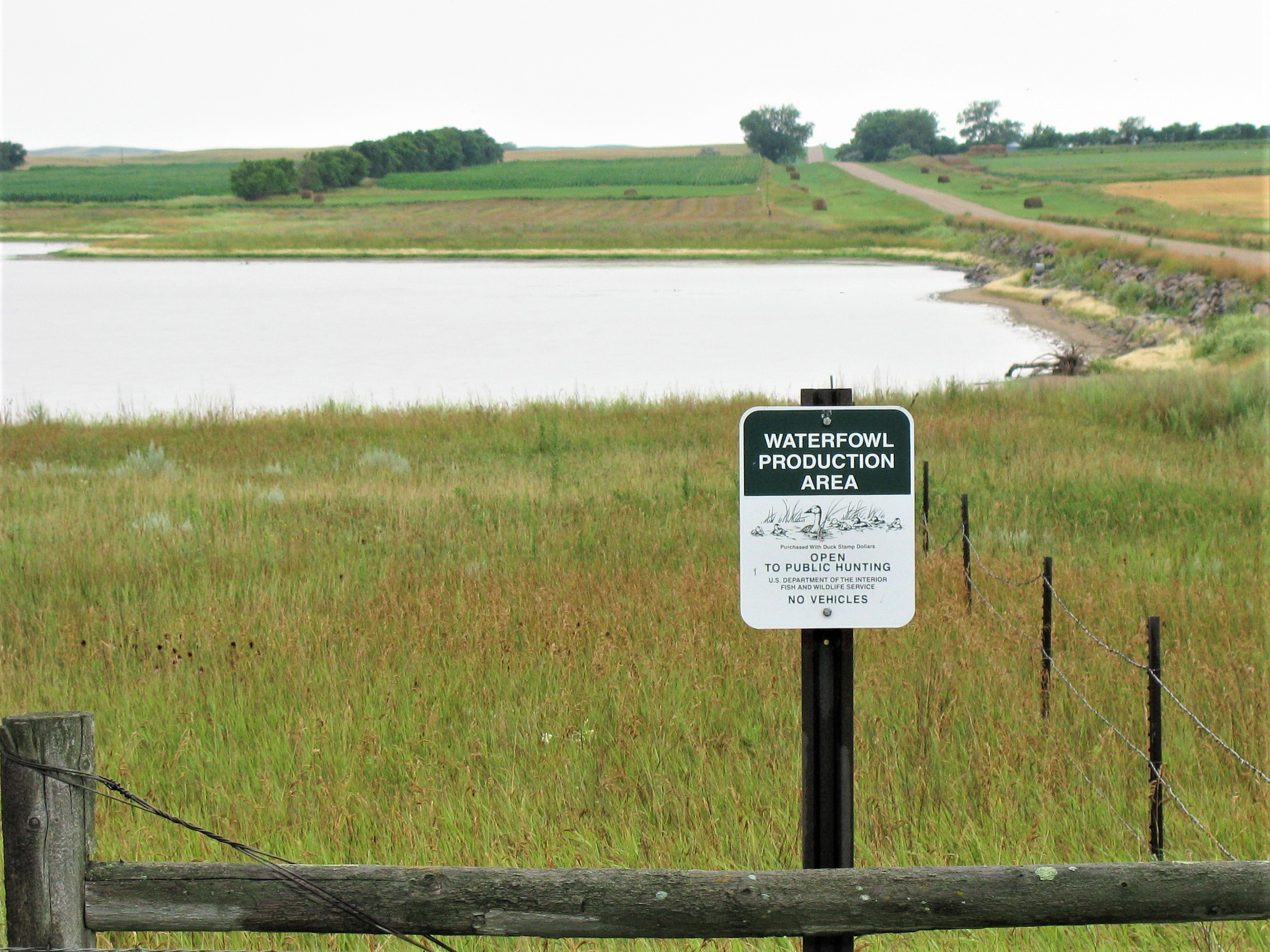 Green and White Waterfowl Production Area sign with a wetland and prairie in the background