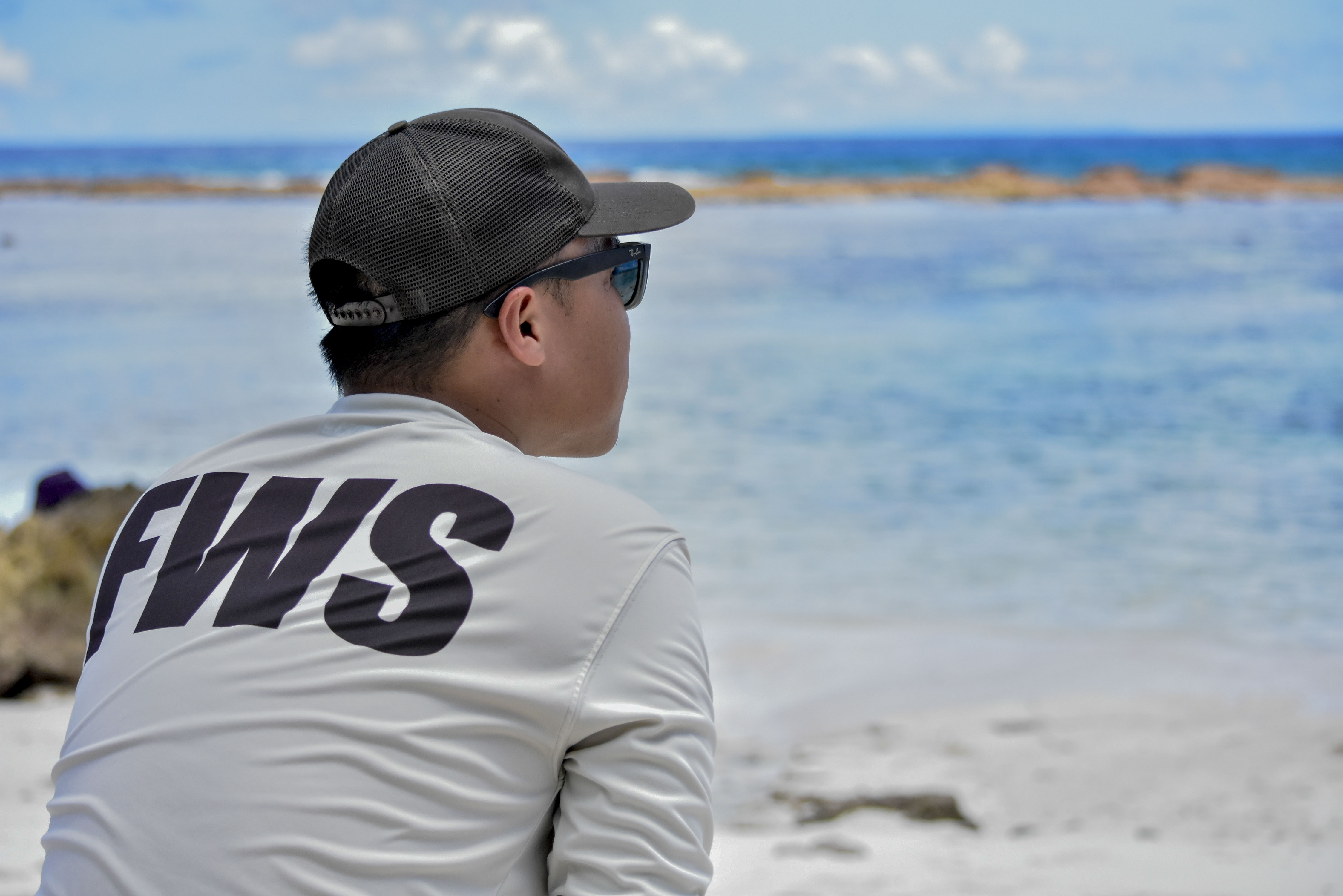A Fish and Wildlife employee wearing a brown FWS shirt and hat, looks out over the reef from the beach. 