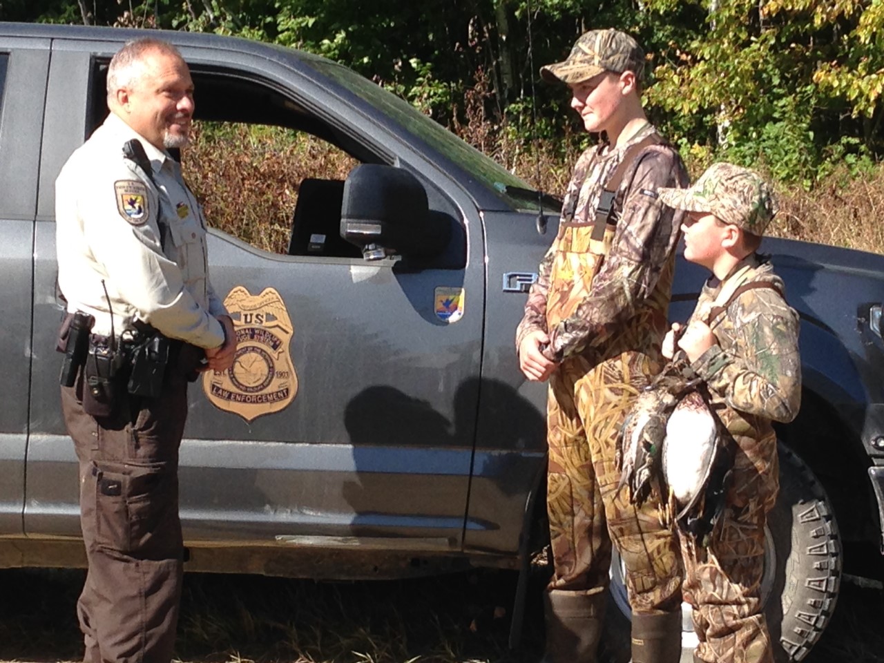 One officer and two youth hunters with their ducks stand near a truck
