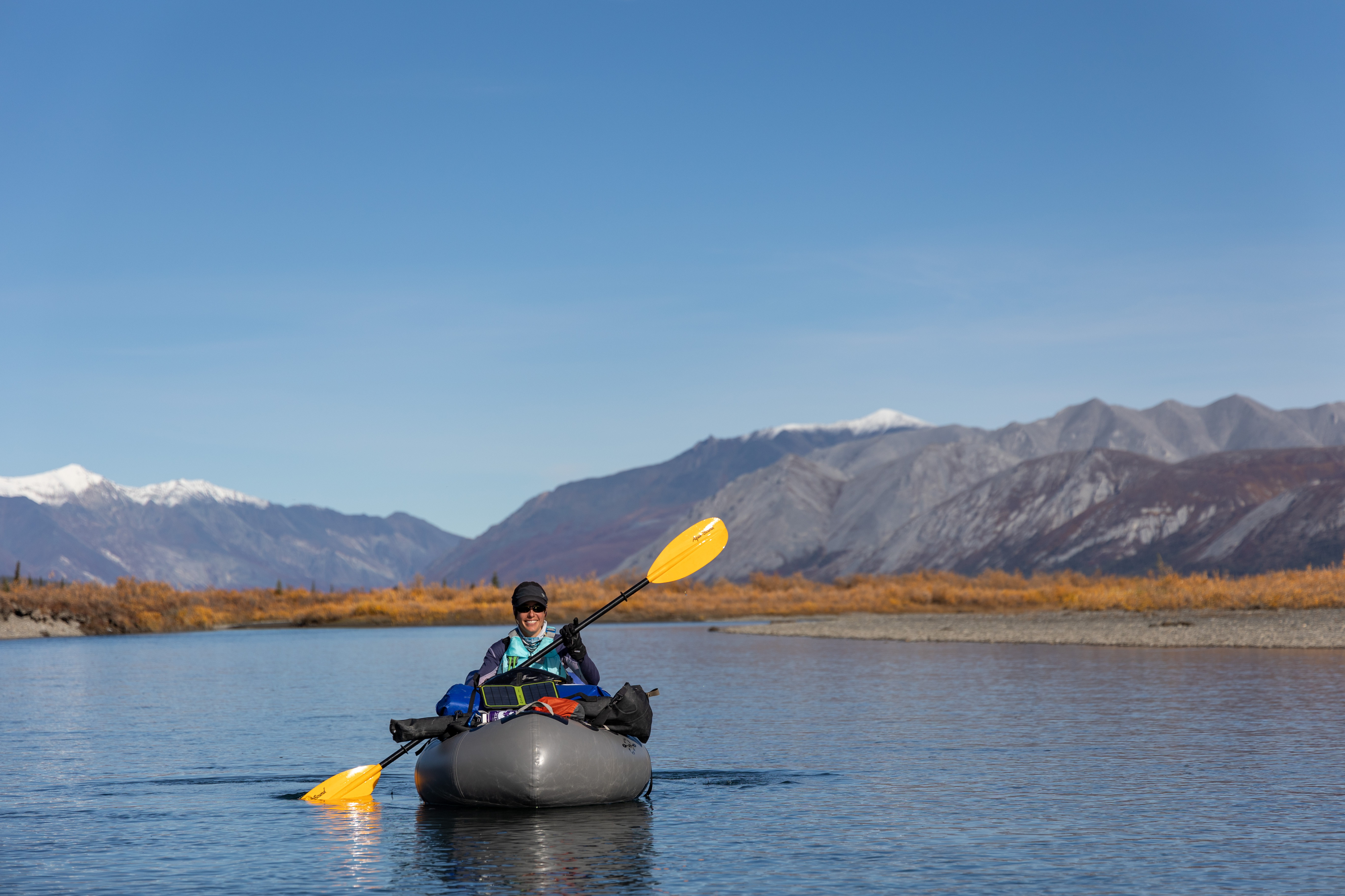 Woman in a small inflatable raft on a river with mountains in background