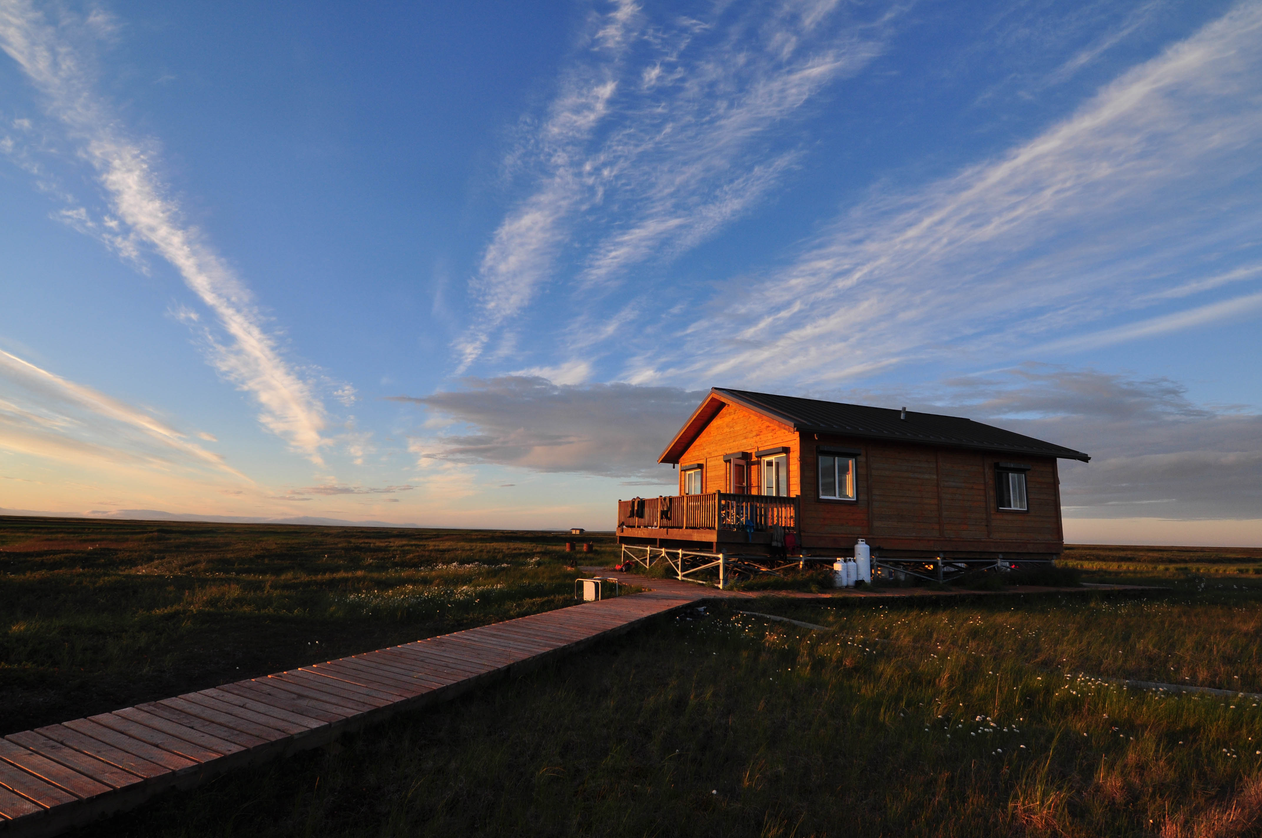 A cabin and boardwalk on tundra at sunset