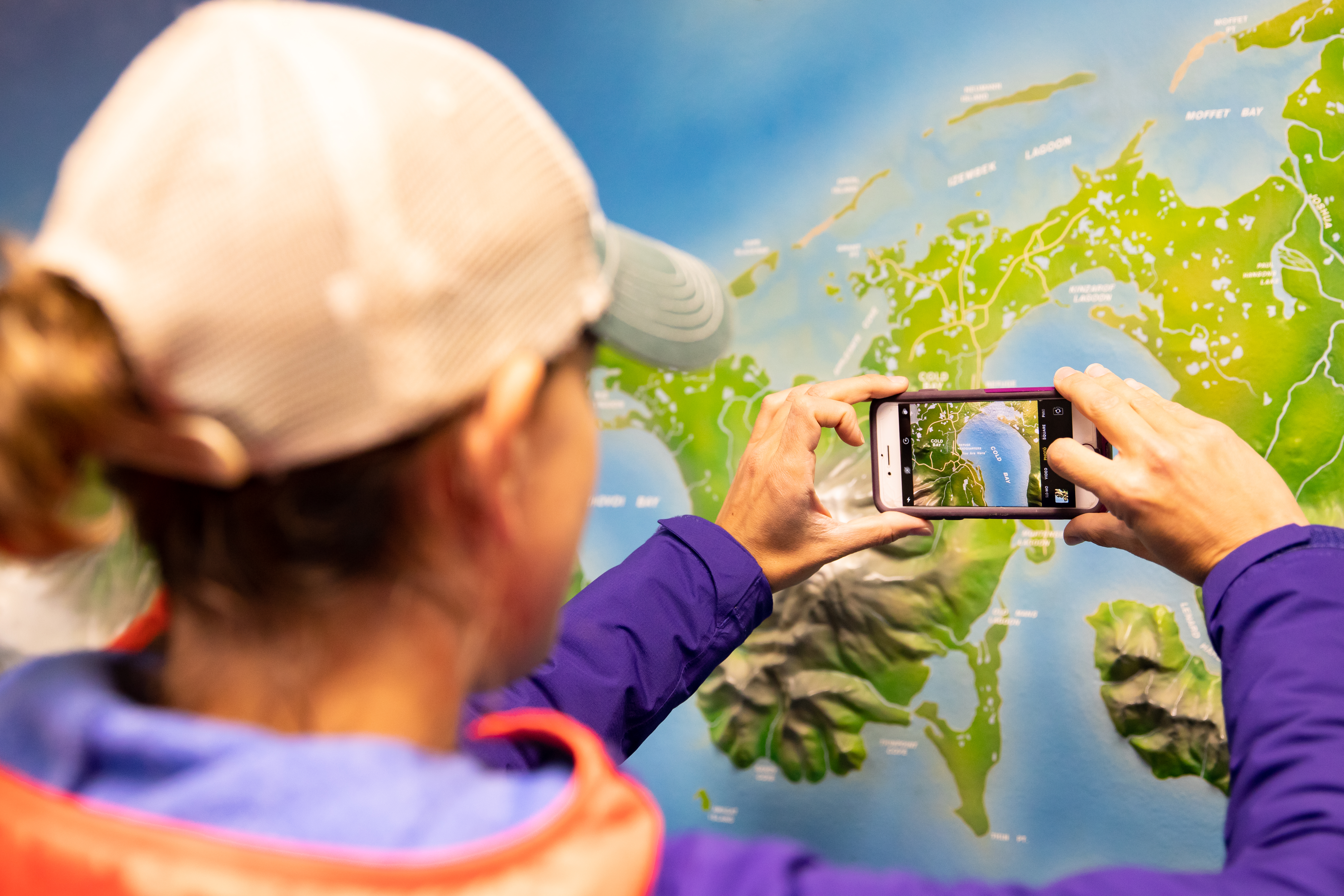 Looking over a woman's shoulder as she takes a photo of a map display with her phone.