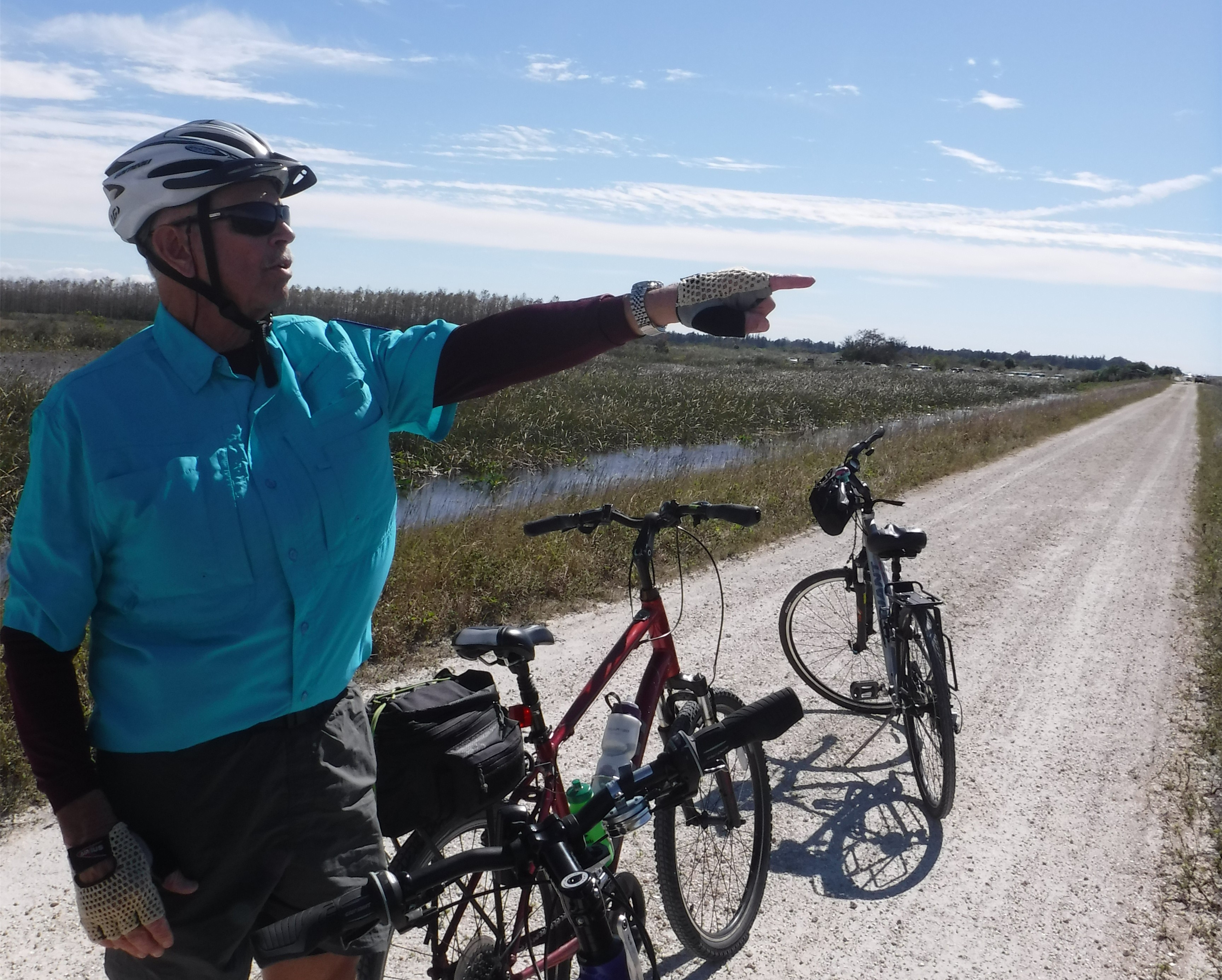 Bike tour leader Lowell Markey stands next to his bike pointing towards the Everglades.