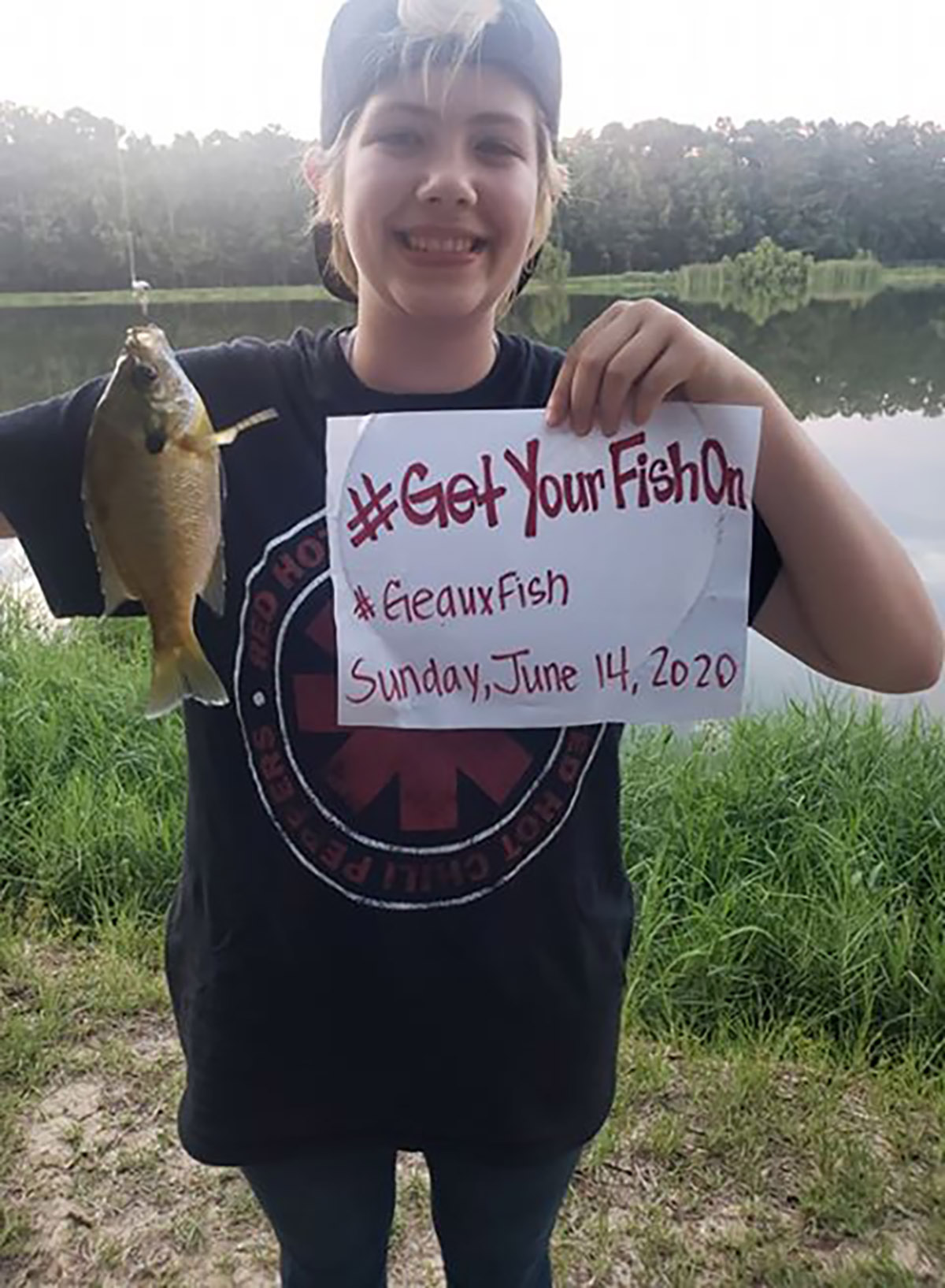 Girl holding a fish and a handwritten dated sign that says #Get Your Fish On and #Geaux Fish