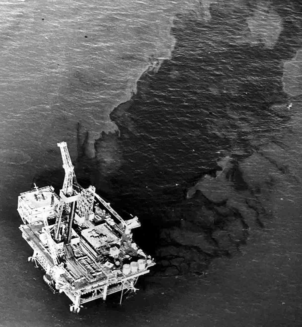 A black and white photo of a boat floating near an oil spill