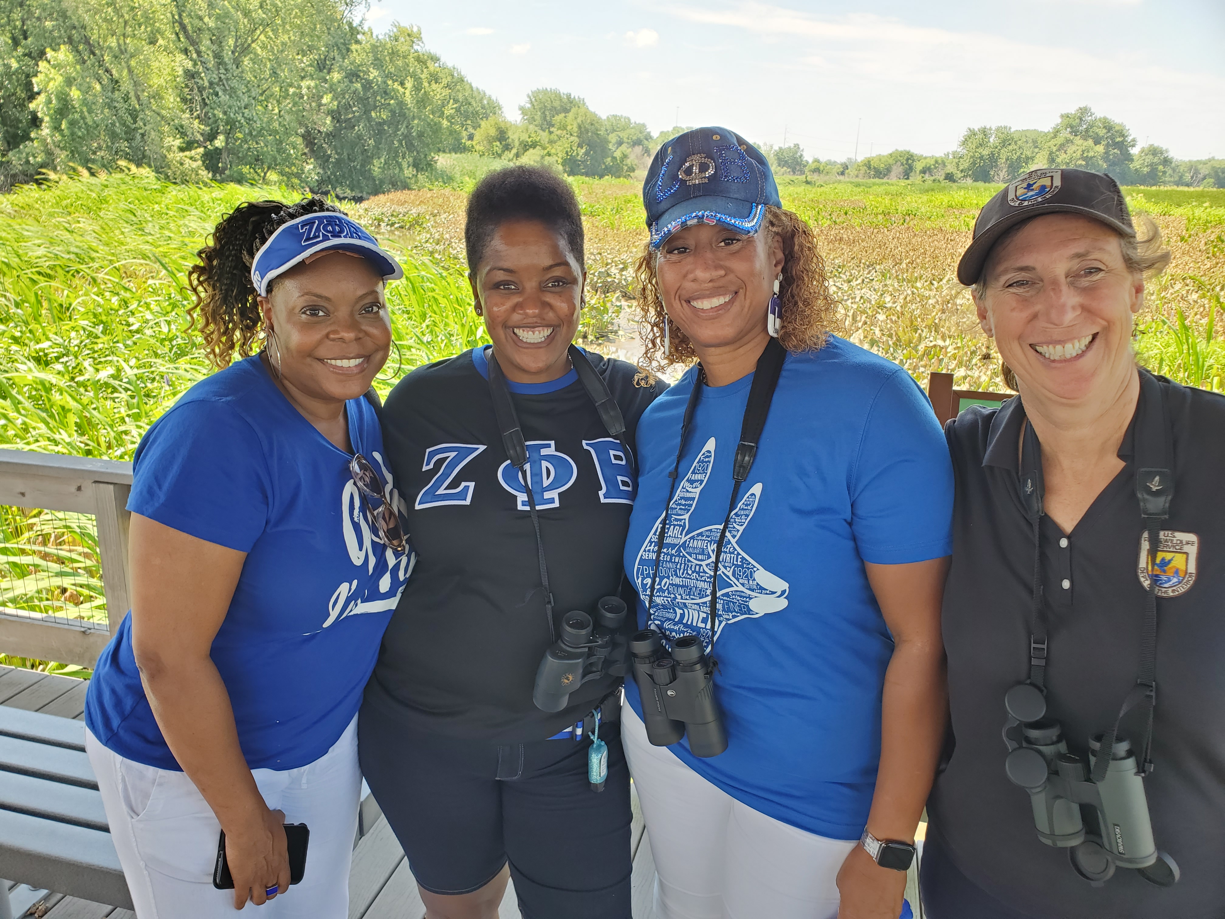 4 women pose outdoors; 3 on left are African American, wear Zeta Phi Beta paraphernalia