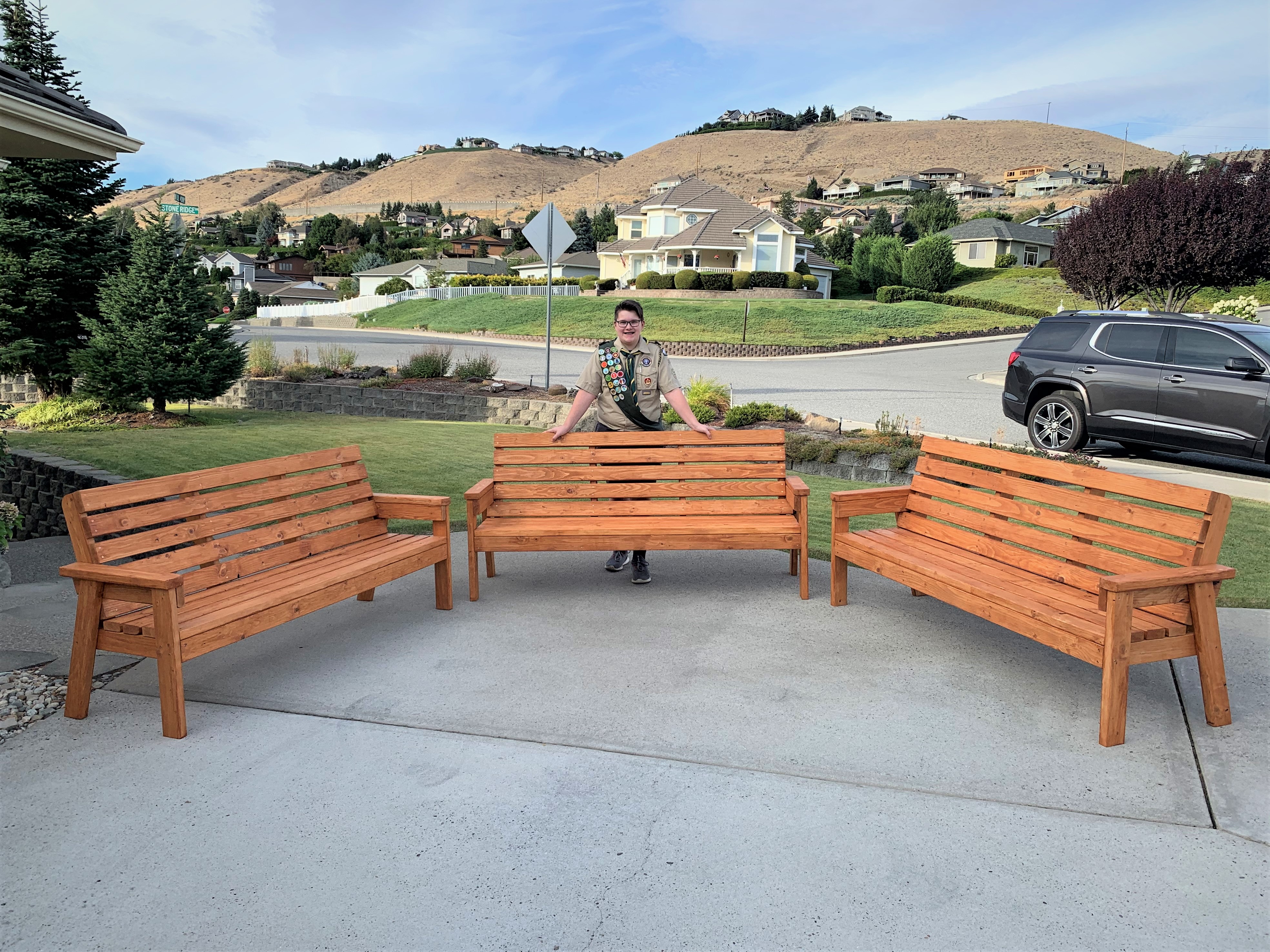 A youth volunteer in his boy scout uniform poses behind the wooden benches he  made for Leavenworth NFH