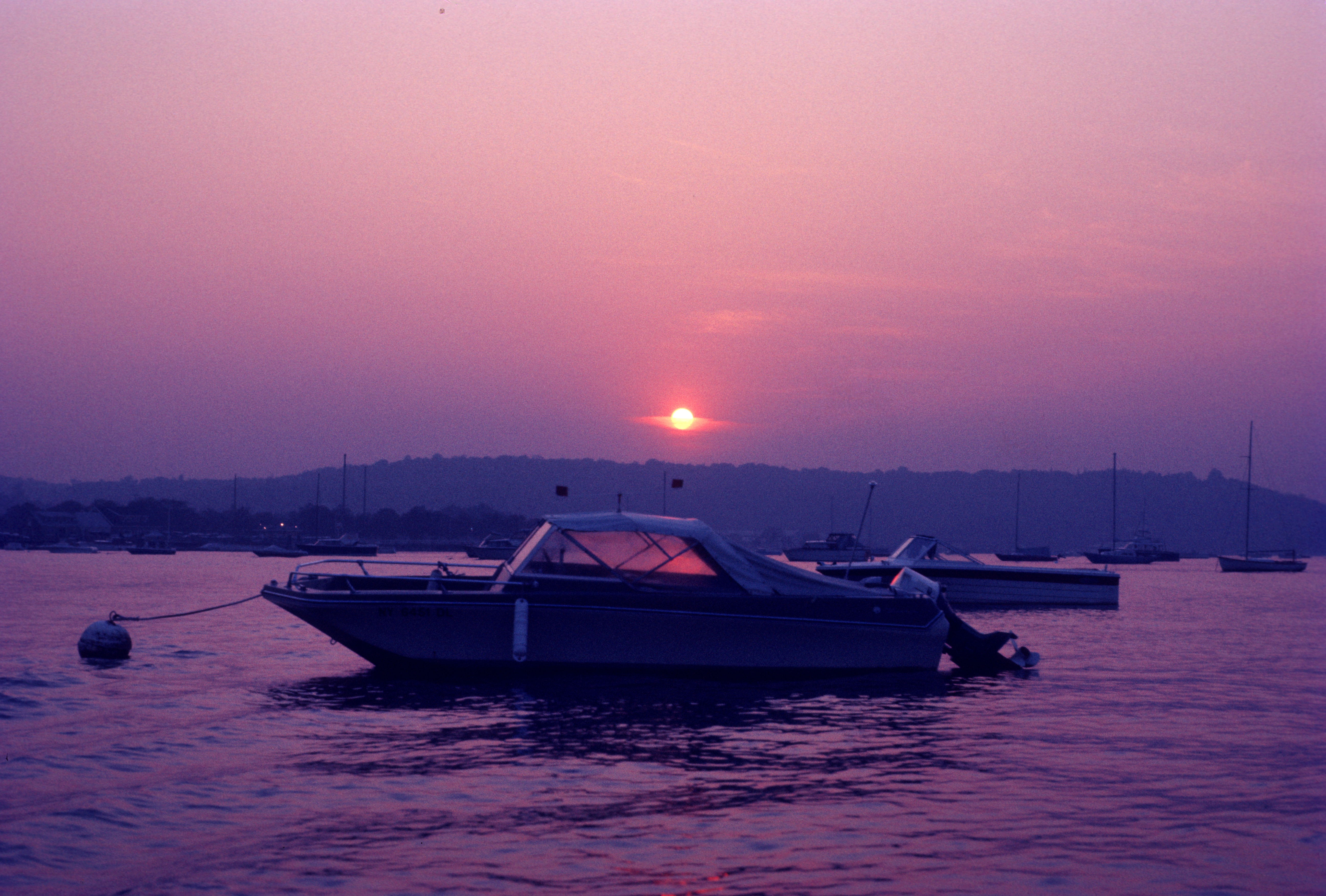 A boat moored offshore is illuminated by a pick sunset
