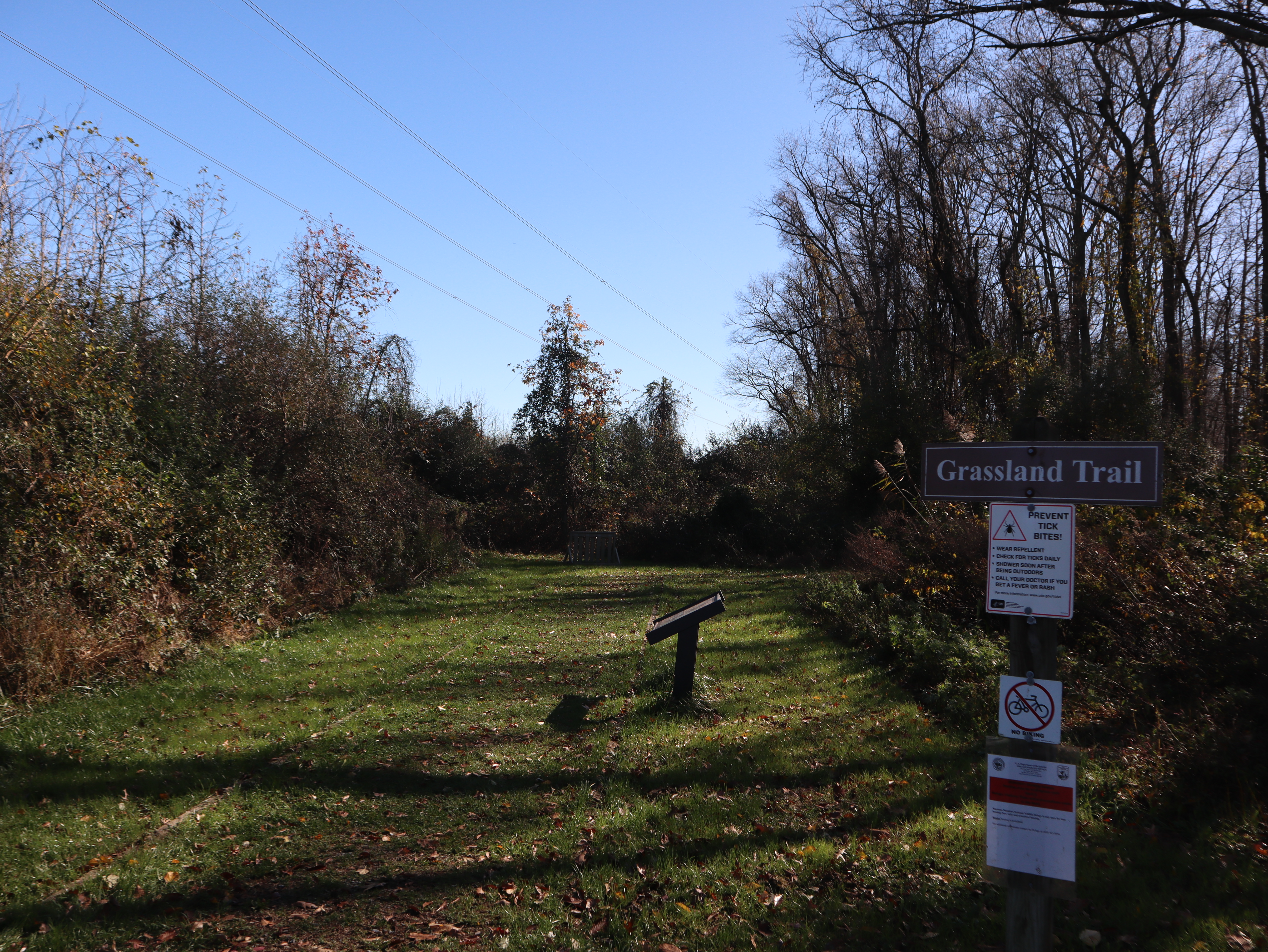 An open trail is shown with informational signs on the right side of the photo. Signs that state the rule, regulations, and name of the trail. 