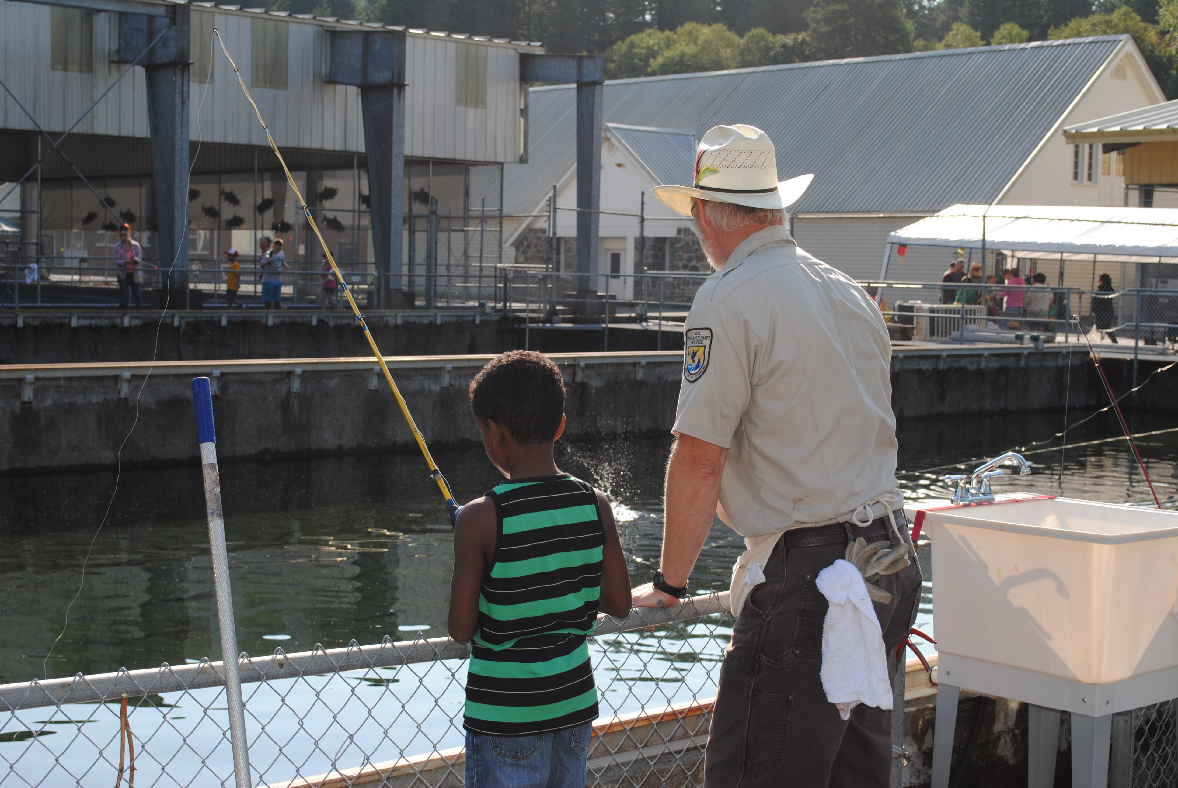 An adult showing a young person to fish over a railing at a fish hatchery.