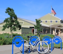 A bicycle rests on a bike rack in front of a green-painted visitor center on a prairie