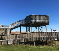 A wooden double decker observation deck with green grass in the foreground and a blue cloudless sky 