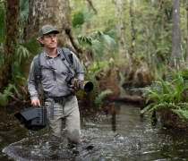 Carlton Ward Jr. is shown wading through a Florida swamp hauling camera equipment.