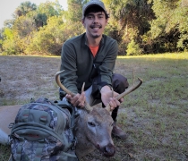 Damon Dawson Jr. kneels in the field, holding onto the antlers of the 6-point buck he harvested on Bulls Island. 