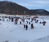 Hundreds of kids ice fishing with their families on a frozen hatchery pond with snow on the ground. 